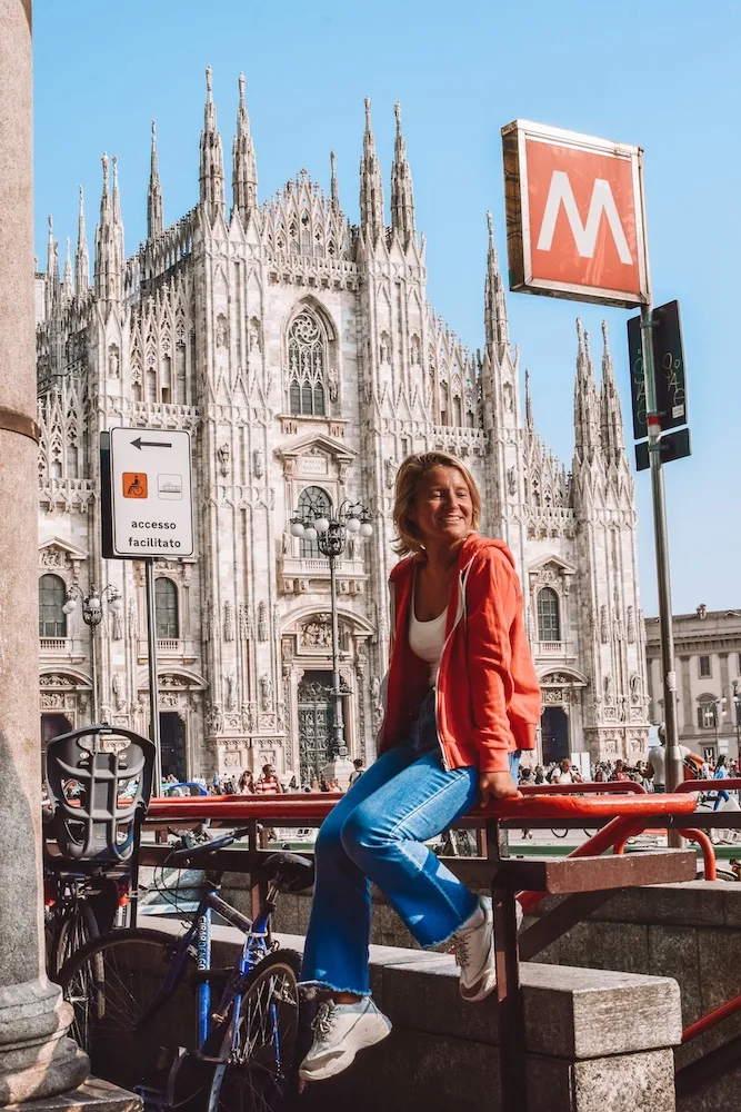 Girl in a red jumper sat on the red railways of the Metro in Milan, with the Duomo Cathedral behind her