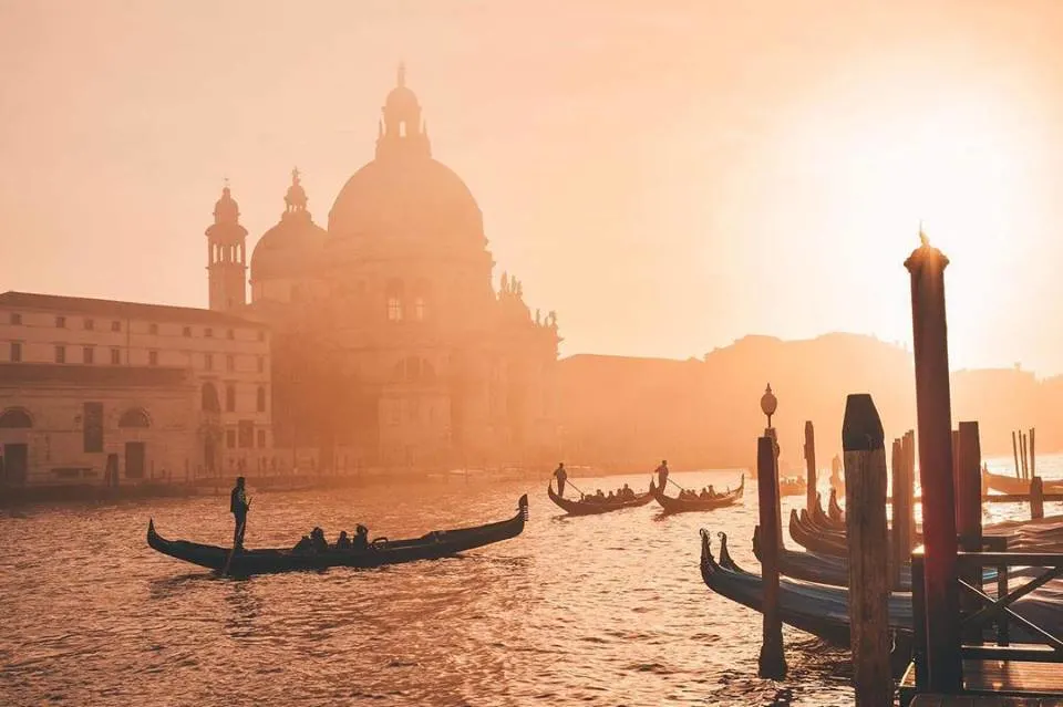 Sunset at the Basilica di Santa Maria della Salute in Venice, with gondola boats cruising in front it