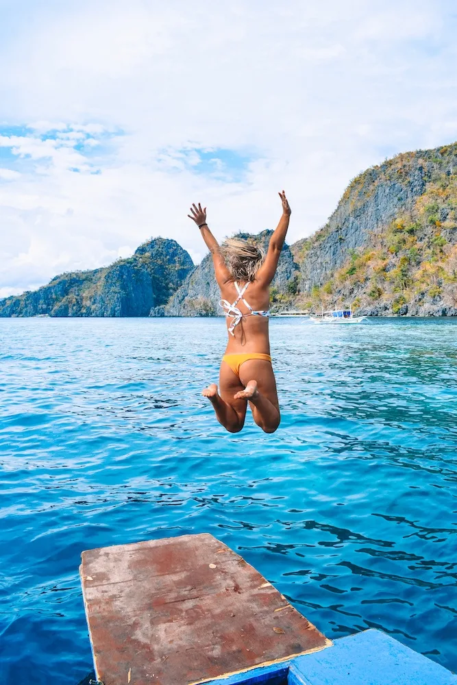 Girl jumping off a boat in Coron, with limestone cliffs in the background