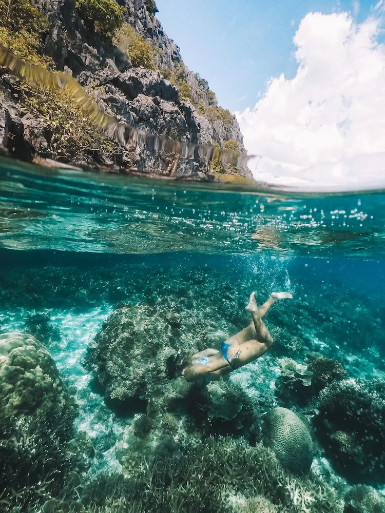 Girl snorkelling in El Nido, Philippines - taken with a GoPro dome, 50/50 with corals under water and steep limestone cliffs over