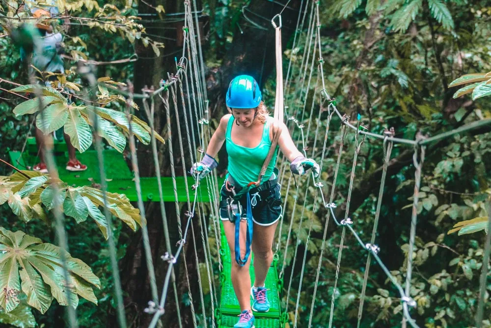 Blonde girl walking across a hanging bridge at the top of rainforest treetops in Tortuguero National Park