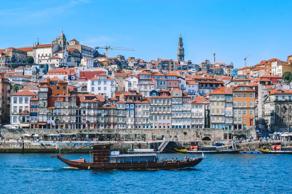 A traditional rabelo boat cruising along the Douro River with the recognisable Porto skyline behind it