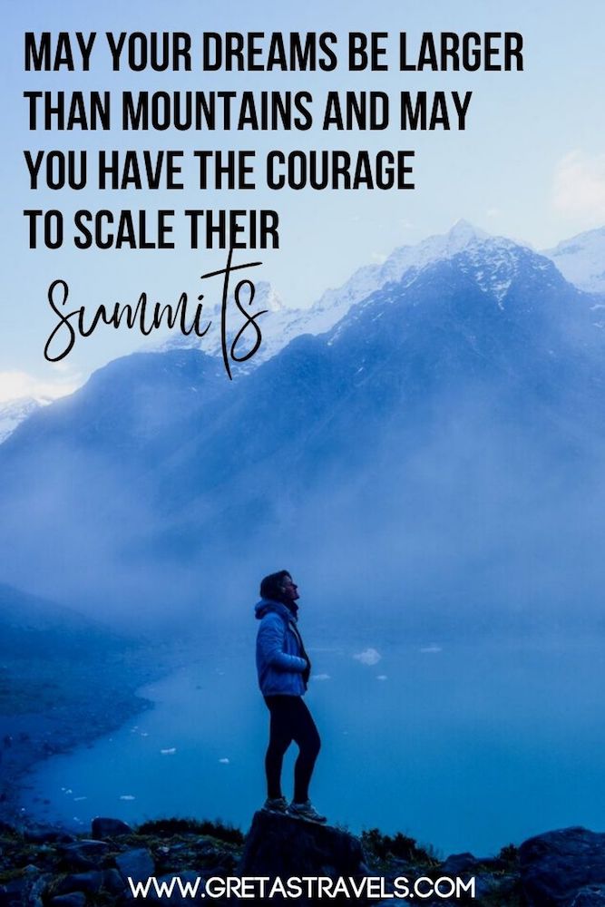 Photo of a blonde girl with a turquoise jacket standing by the glacier lake of Hooker Valley Track with the mountains behind her and text overlay saying "May your dreams be larger than mountains and may you have the courage to scale their summits"