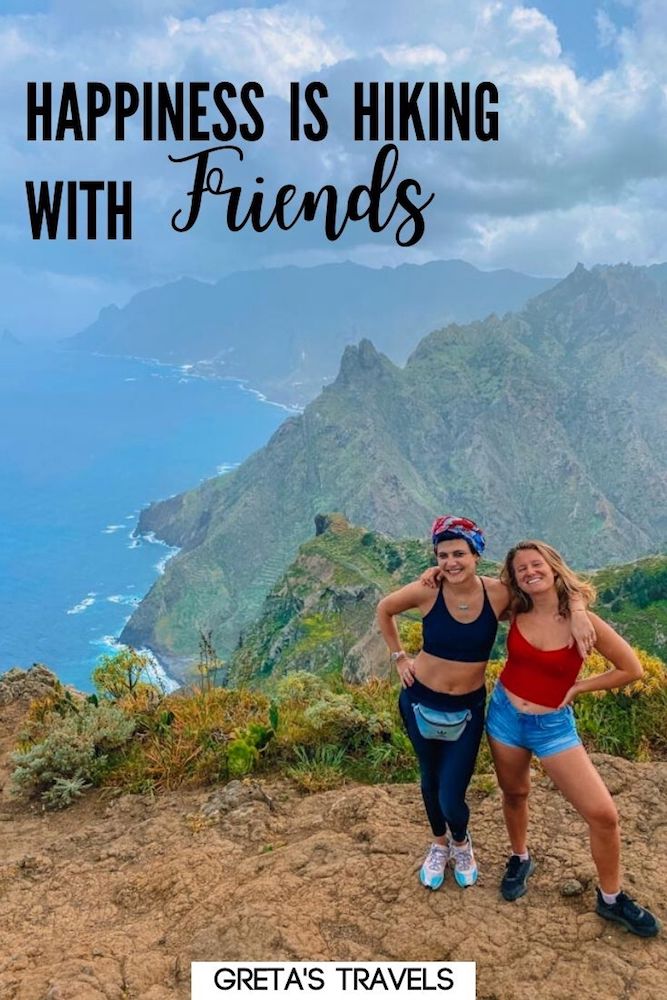 Photo of two girls standing on top of a cliff in Anaga, Tenerife, with text overlay saying "Happiness is hiking with friends"