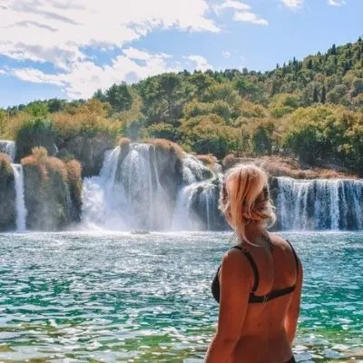 Blonde girl in a black bikini standing in front of the waterfalls of Krka National Park