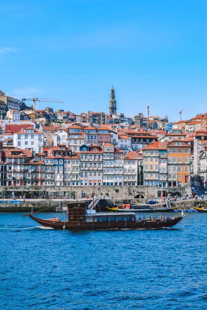 A traditional rabelo boat cruising along the Douro River with the Porto cityscape behind it