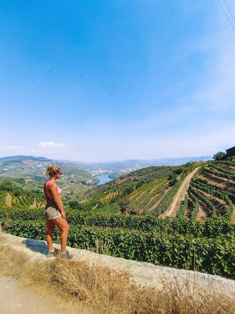 Blonde girl in a pink top and shorts standing in front of the vineyards of the Douro Valley, Portugal