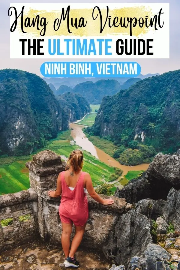 Photo of a blonde girl in a pink jumpsuit standing at the top of Hang Mua Caves Viewpoint enjoying the view over the mountains, rice fields and river of Ninh Binh, with text overlay saying "The ultimate guide to Hang Mua Viewpoint in Ninh Binh, Vietnam!"